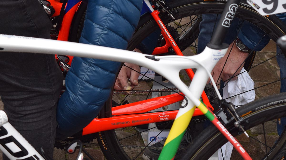A Groupama-FDJ mechanic applies a waxy chain lube by hand to a riders bike at the race start
