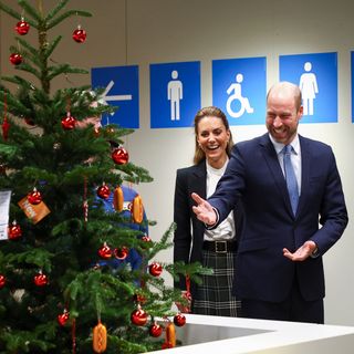 Prince William and Princess Kate standing in front of a Christmas tree and laughing