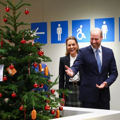 Prince William and Princess Kate standing in front of a Christmas tree and laughing