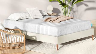 The Leesa Hybrid memory foam mattress on a light gray fabric bed base next to a wicker chair