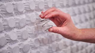 A hand holds a bare microcoil in front of a individually-wrapped microcoils on a factory floor. 