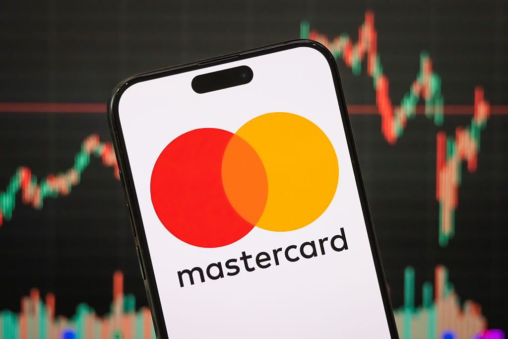 The logo of Mastercard Incorporated is displayed on a smartphone screen, with the company's latest stock market performance on a chart in the background