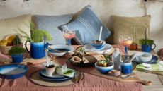 outdoor dining table with rust linen table cloth and bright blue bowls and plates 