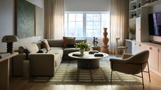 Image of a modern living room with a sage green sectional sofa, a round coffee table, a green rug, built-in shelving, and an accent chair.