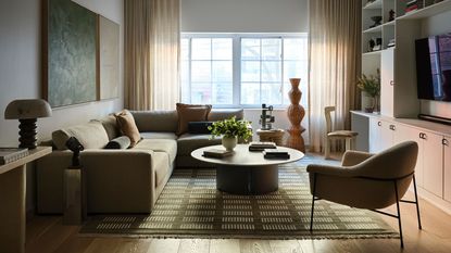 Image of a modern living room with a sage green sectional sofa, a round coffee table, a green rug, built-in shelving, and an accent chair.