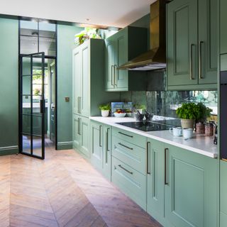 A sage green kitchen with hardwood floors and brass hardware