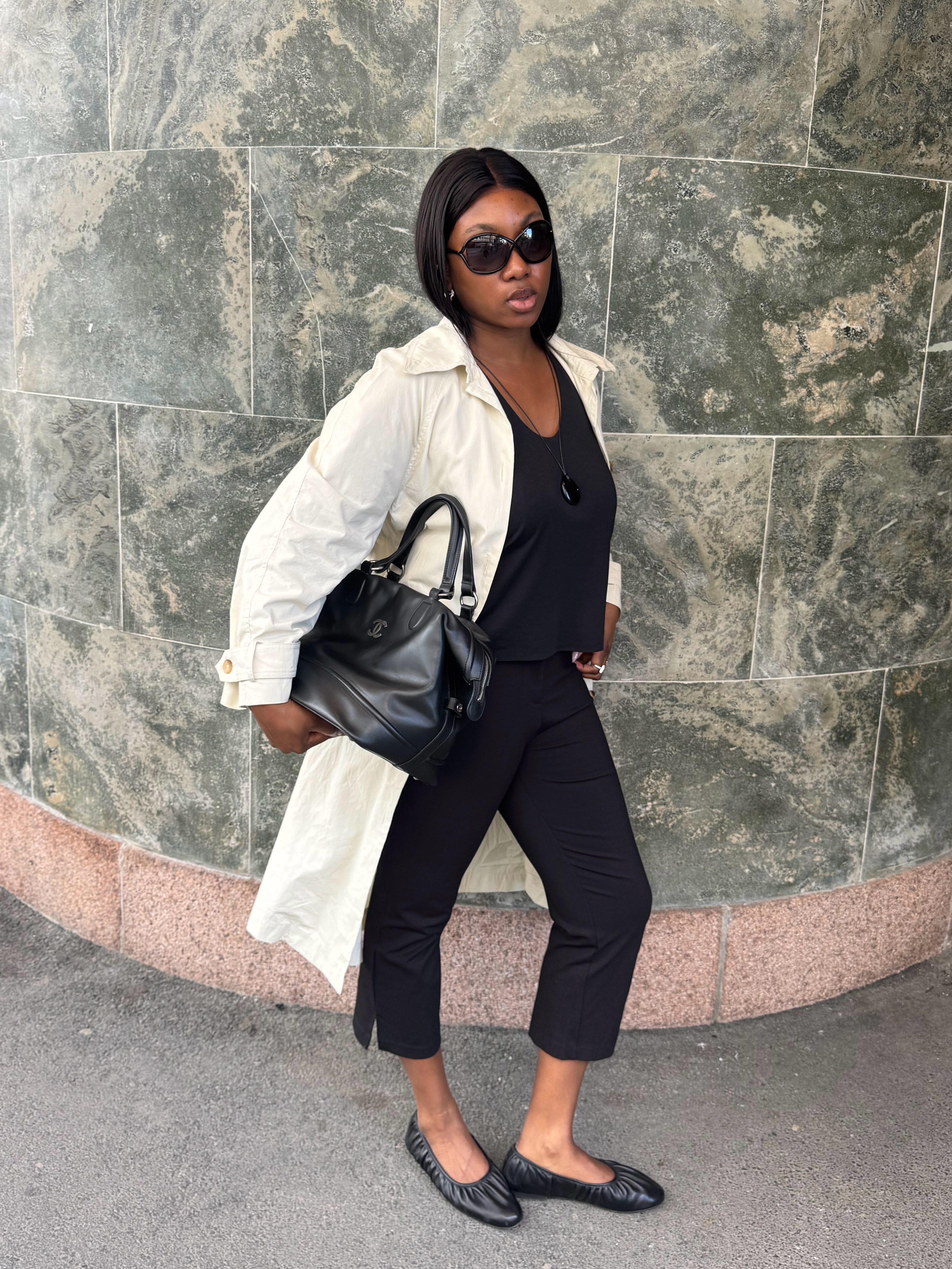 An image of an influencer wearing a light beige trench coat with a black top, capris and ballet flats