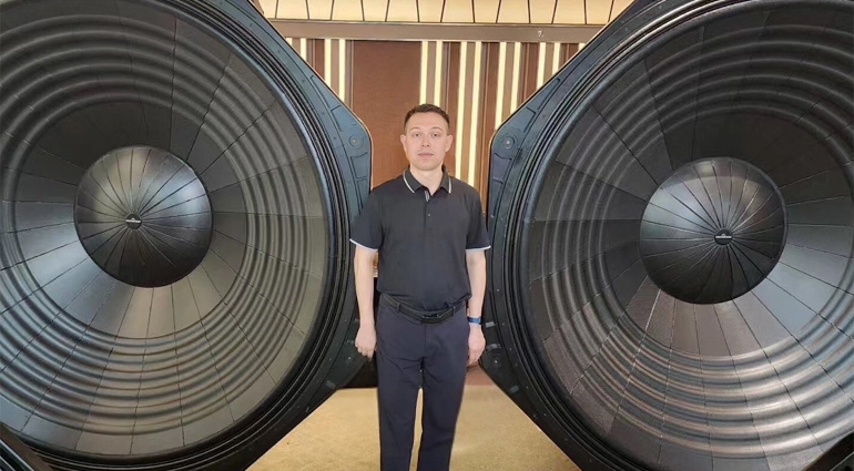 A man standing between two absolutely enormous 100-inch subwoofer drivers