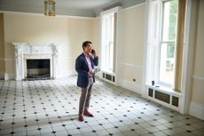 Smartly dressed real estate investor or agent standing in spacious empty room of house for sale talking on cell phone.