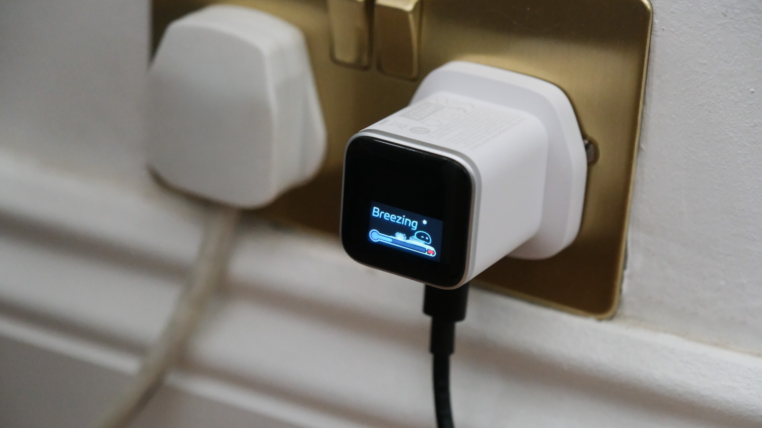 Anker Nano Charger plugged into a wall socket, with its smart display showing a &amp;ldquo;Breezing&amp;rdquo; charging status.