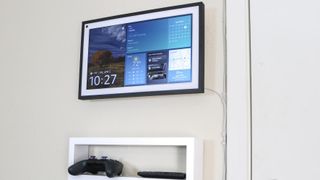 An Amazon Echo Show 15 mounted to a wall in the kitchen with a shelf underneath it