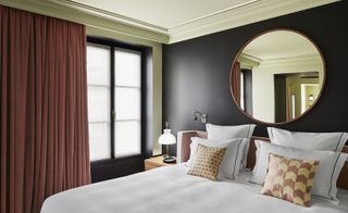 hotel bedroom with black wall and circular mirror behind the bed