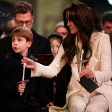 Kate Middleton wearing a white suit and adjusting Prince Louis's candle at a church service