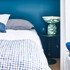 A bedroom with a dark blue wall and blue and white bedding on the bed