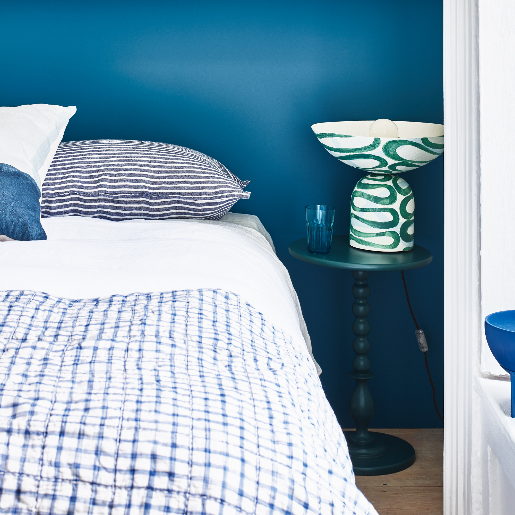 A bedroom with a dark blue wall and blue and white bedding on the bed