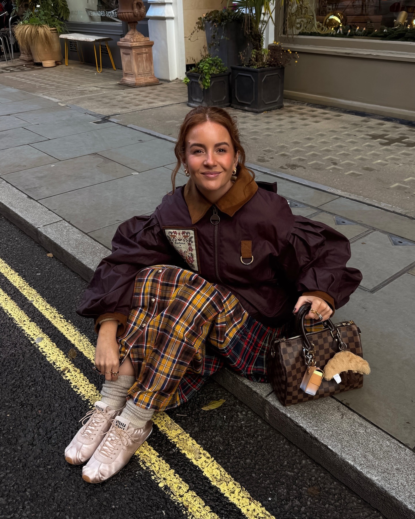Influencer @rebeccaferrazwyatt wears Miu Miu satin elasticated trainers with a plaid skirt and burgundy jacket.