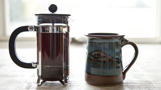 French press and cup sitting on table with coffee in it