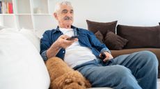 Man watching tv holding remote on sofa with dog