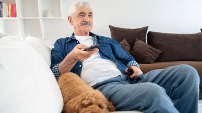 Man watching tv holding remote on sofa with dog