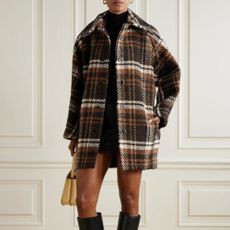 Woman wearing autumn brown and white chequered coat, yellow bag, and black boots, stood in front of white wall.