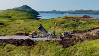 A truck dumps gravel next to a backhoe.