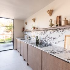 Oak kitchen with black and white marble worktop and splashback up to an open shelf with wicker wall lights on the wall above