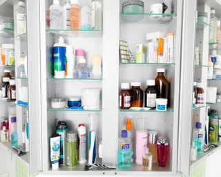 Cluttered, colourful bathroom medicine cabinet with doors open