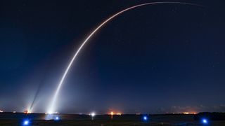 A rocket streaks into space as an arc of light at night in a long exposure