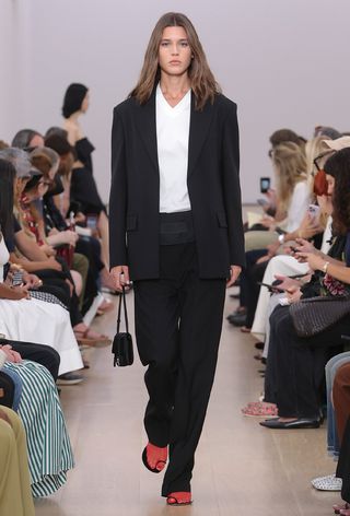 model wearing black suit with white button-shirt and red sheer socks and black sandals