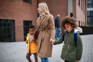 Two children walking to school either side of their mum