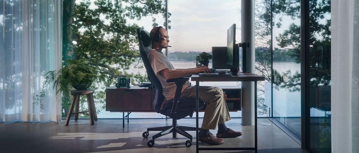 A wide shot showing a man sitting at the Fractal Refine gaming chair in front of a desk