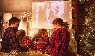A family of four, all dressed in matching tartan Christmas pyjamas, watching a projector film together.