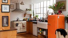 Orange Smeg fridge in a white kitchen with lots of plants