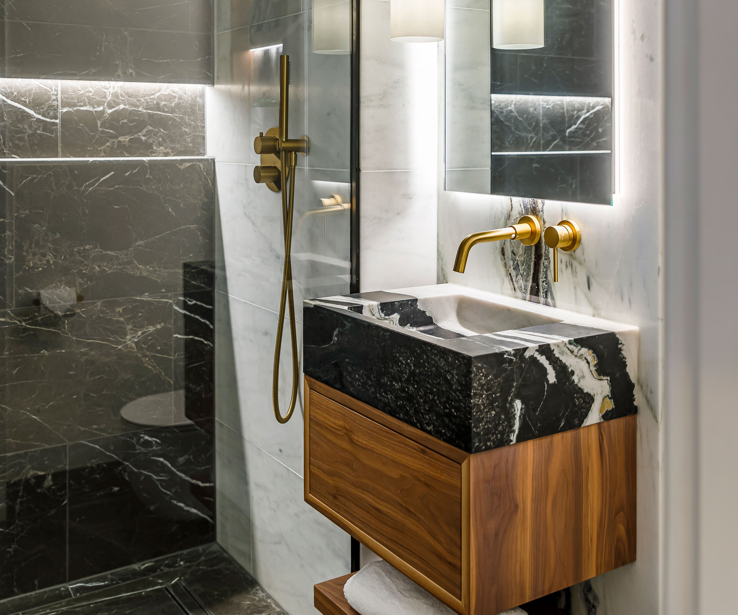 Panda marble basin on wooden vanity unit with brass taps and walk-in shower with black marble wall tiles