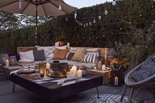 garden sofa with lots of cushions, throws and lit by garden lighting and lanterns