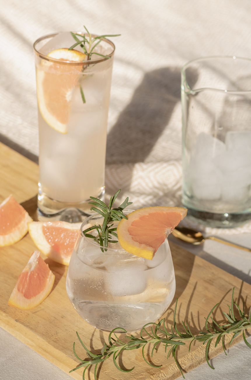 Two glasses on a wooden board with drinks over ice
