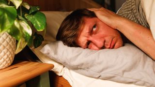 A man sleeping on his side covering his ears and looking frustrated