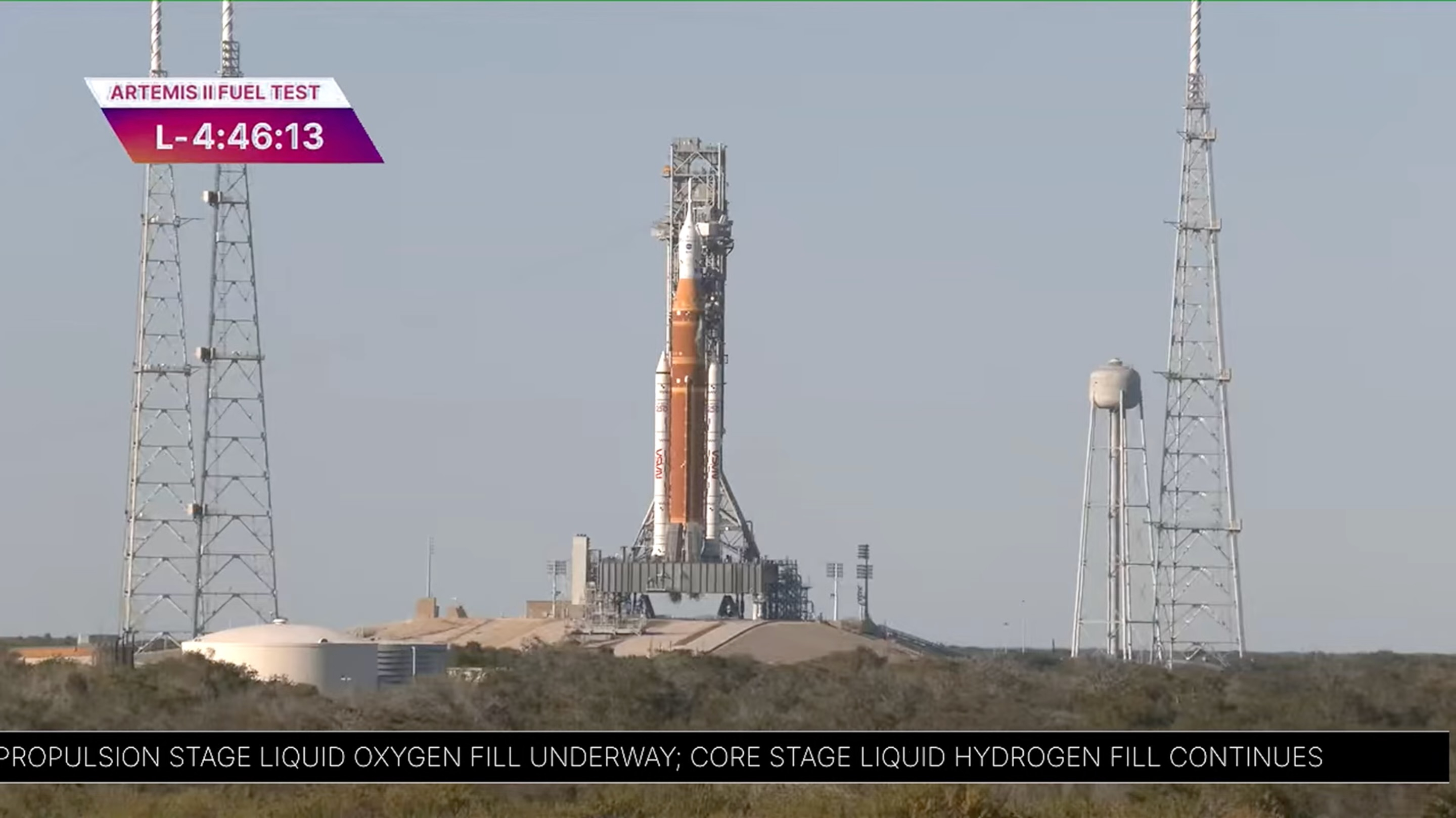 long-range photo of an orange and white rocket on a launch pad, with blue sky in the background