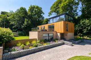 A three-storey self build with a balcony and a block paved drive and flower beds around the drive