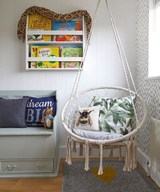 childrens room with hanging hammock rope chair, wall mounted book shelf with snake toy, wallpaper and floor rugs with blue wooden seat