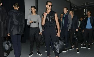Male model wearing black, holding accessories