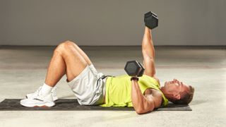 a man lying on a mat performing dumbbell presses
