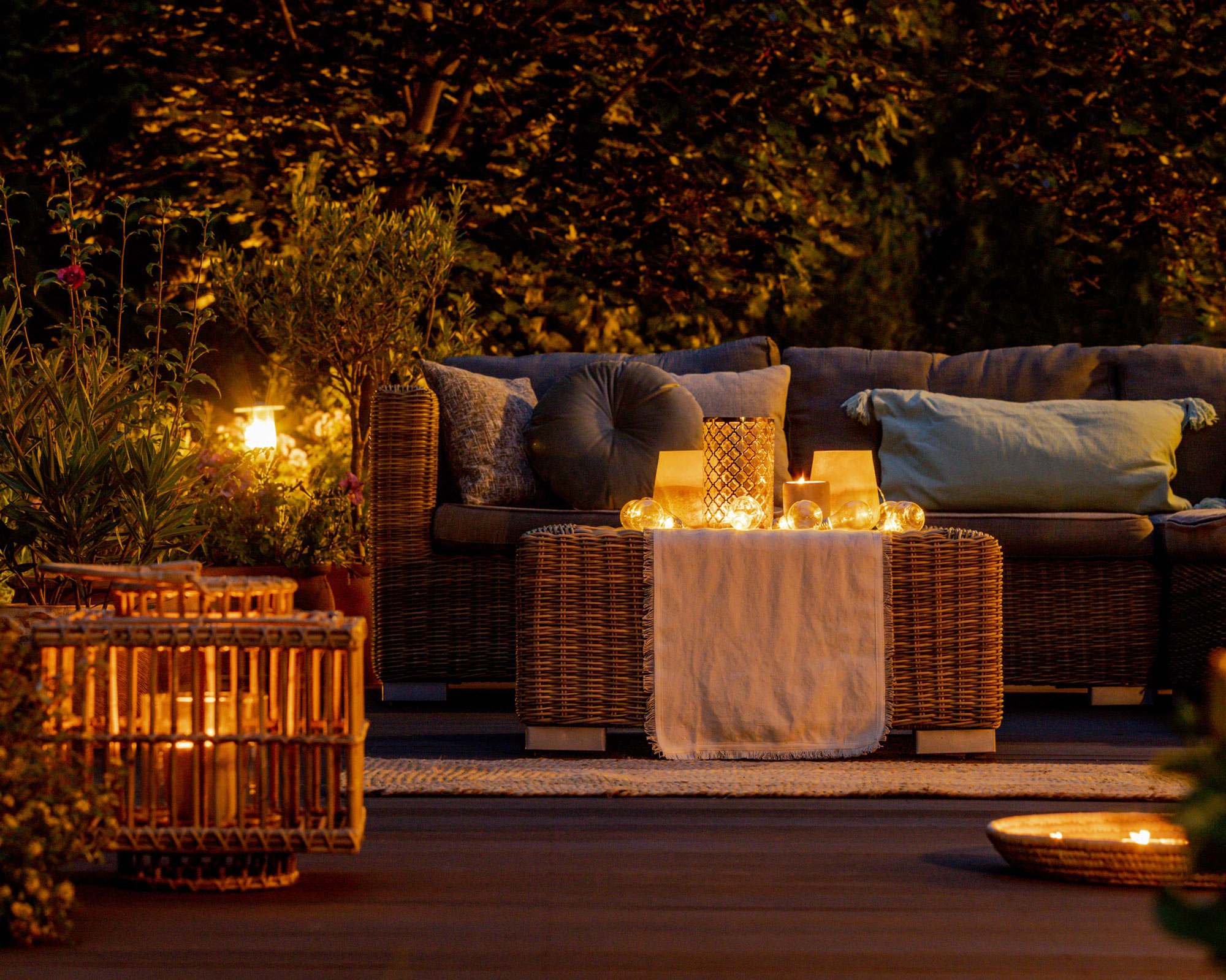 patio at night with lighting and candles, garden sofa with cushions and table