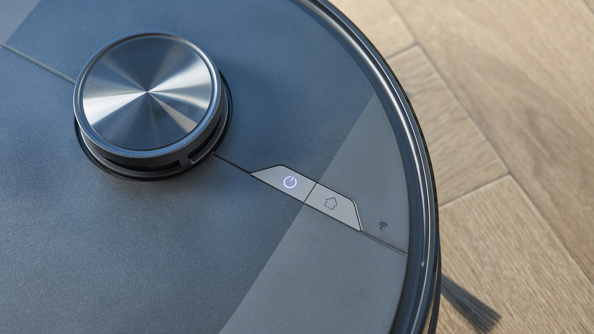 a rechargeable robot vacuum and mop in black by ultenic is photographed on a hardwood floor with a blue wall and a burnt orange terracotta and white striped rug