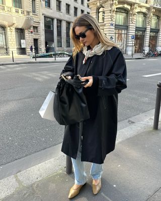 Anne-Laure Mais wearing a black car coat with light jeans and camel pumps.