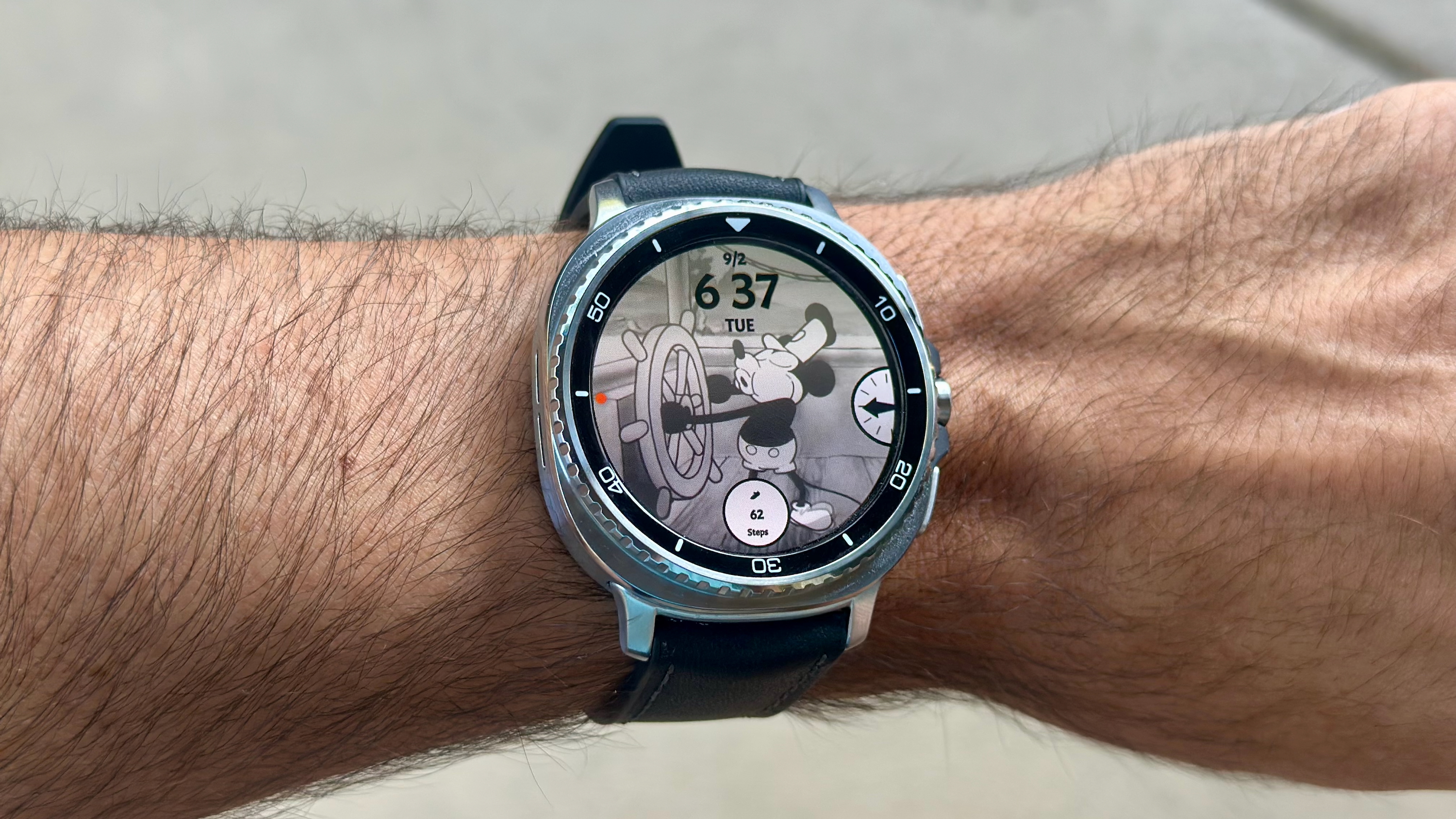 The Samsung Galaxy Watch 8 Classic on a person's wrist, showing a custom watch face from Facer of Steamboat Willy.