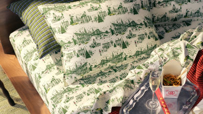 Brooklinen green Tree Top Toile Washed Percale Sheet Set styled with a chrome dinner tray holding a champagne flute and Chinese takeout.