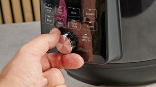 a black instant pot with a dial and touchpad is photographed against a blue background