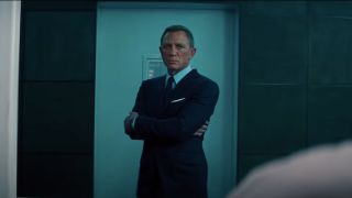 Daniel Craig stands with arms crossed looking disturbed in No Time To Die.