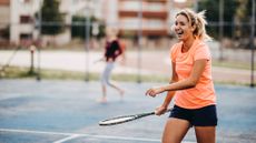 Woman holding tennis racket walking on tennis court. Her mouth is open and she is smiling